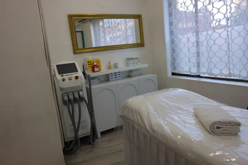 A treatment room at The Contour Hub, with a treatment bed and a device on a stand beside a curtained window.